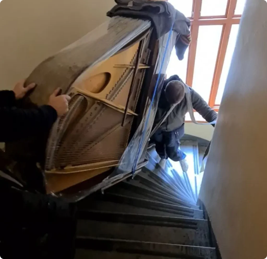 Flygel på högkant bärs nedför en trappa av två personer