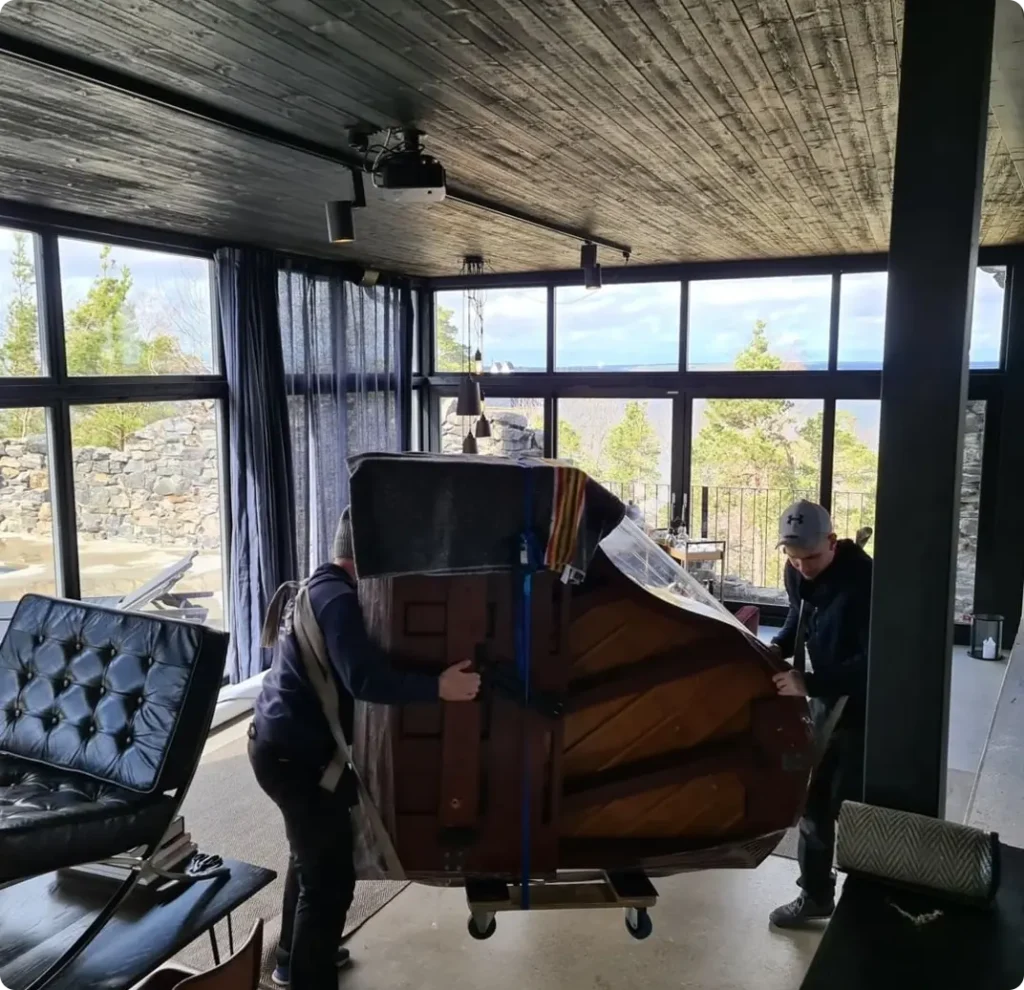 Två bärare med ett piano på högkant i ett rum med stora fönster